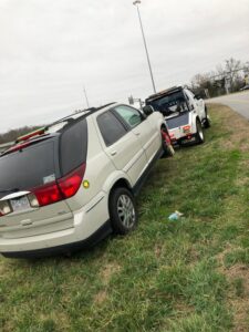 A white SUV partially off the road, being recovered by a J & G Towing, LLC truck in Greensboro, NC.