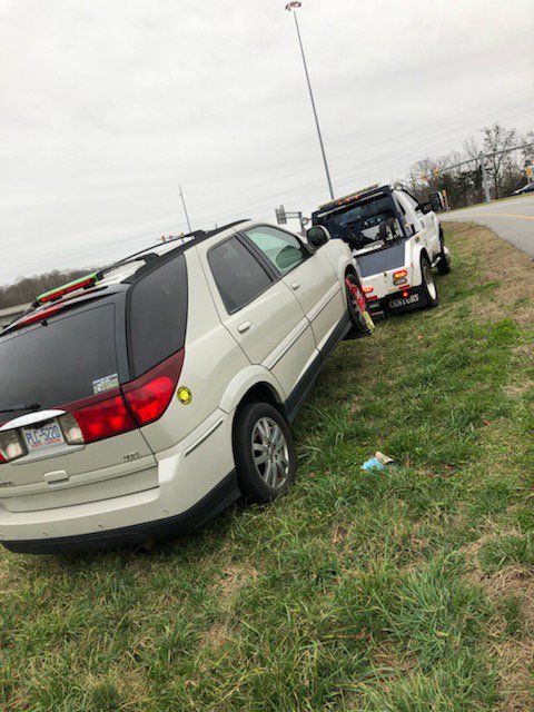 A white SUV partially off the road, being recovered by a J & G Towing, LLC truck in Greensboro, NC.