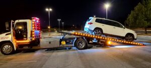 A white SUV being towed on a flatbed tow truck at night by Ibanez Towing Service LLC in San Jose, CA.