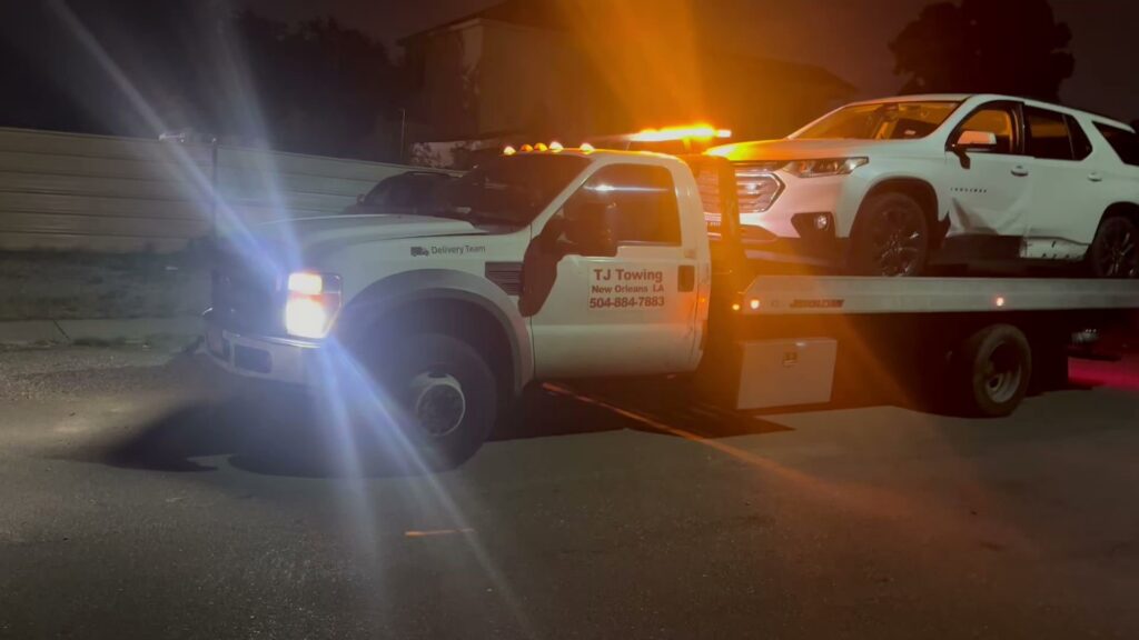 TJ Towing LLC flatbed truck towing a white SUV at night with emergency lights on in New Orleans, LA.