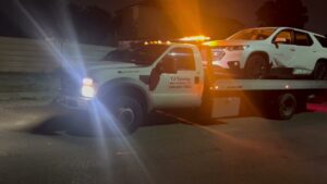 TJ Towing LLC flatbed truck towing a white SUV at night with emergency lights on in New Orleans, LA.