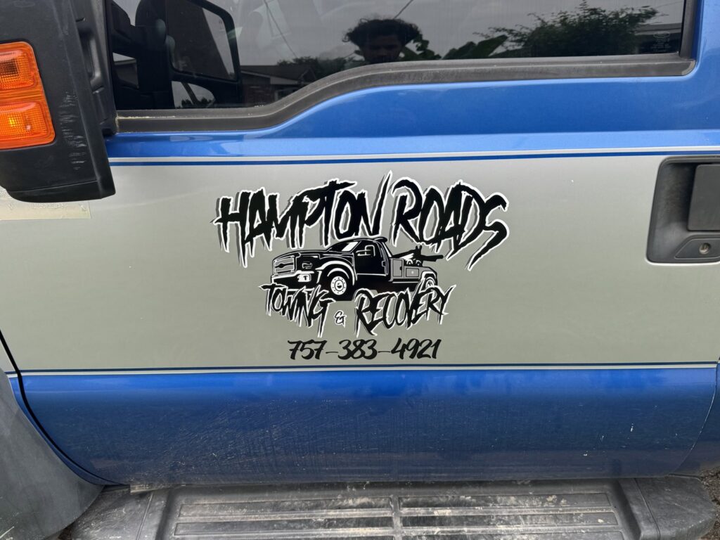 A white SUV on a flatbed tow truck, towing a damaged white sedan behind it by Hampton Roads Towing Services in Chesapeake, VA.