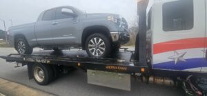 A white flatbed tow truck from Advance Towing & Recovery hauling a grey pickup truck in Columbus, GA.