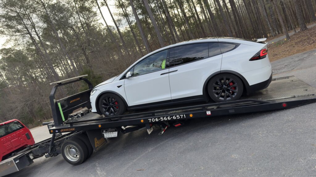 A white flatbed tow truck from Advance Towing & Recovery hauling a white Tesla Model X in Columbus, GA.