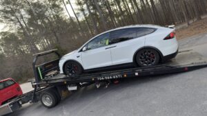 A white flatbed tow truck from Advance Towing & Recovery hauling a white Tesla Model X in Columbus, GA.