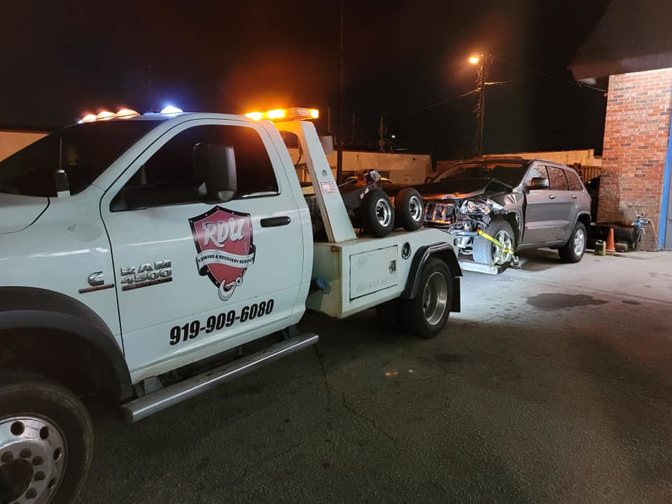 A white tow truck from RDU Towing & Recovery Services towing a damaged Jeep Grand Cherokee in Raleigh, NC.