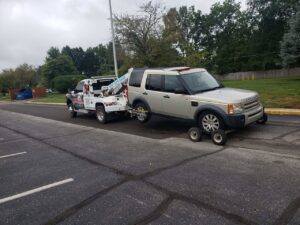 A white tow truck towing a gold SUV using a wheel lift and dollies, providing towing services by JR's Services and Recovery, LLC in Indianapolis, IN.