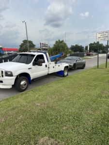 A white No Limit Towing truck actively towing a grey sedan on a street in Orlando, FL.