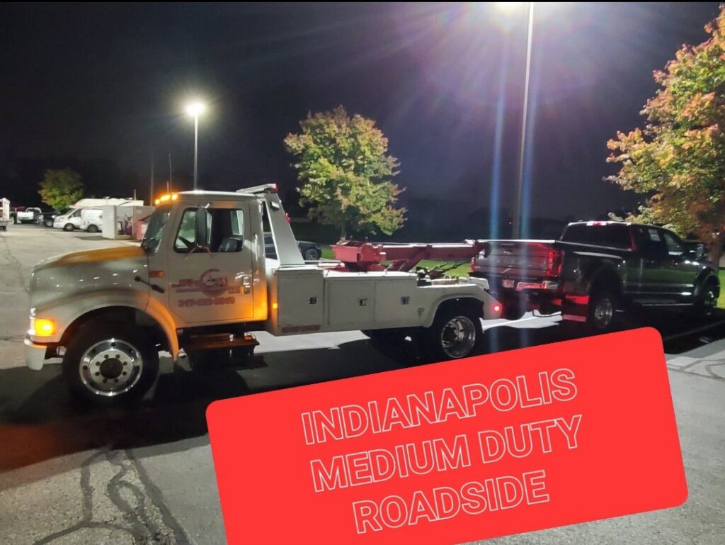 A white tow truck towing a dark pickup truck at night, providing medium-duty roadside assistance by JR's Services and Recovery, LLC in Indianapolis, IN.