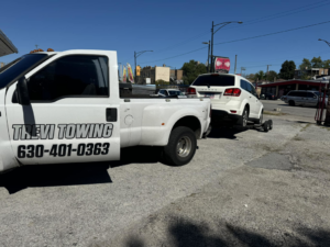 A white Trevi Towing llc truck towing a white SUV with a dolly in Chicago, IL.