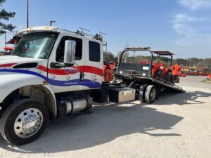 A white flatbed tow truck from Advance Towing & Recovery transporting a small orange tractor in Columbus, GA.