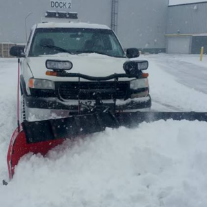 A white commercial snow plow truck actively clearing snow from a large area for 3-D Lawncare & Landscaping in Flint, MI.