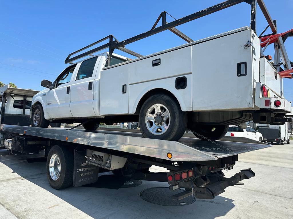 A white utility truck being transported on a flatbed tow truck by Ledesma's Towing in San Diego, CA.