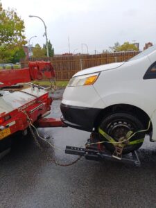 A white van being towed by a red tow truck using a wheel lift system, provided by Buffalo Towing Services in Buffalo, NY.