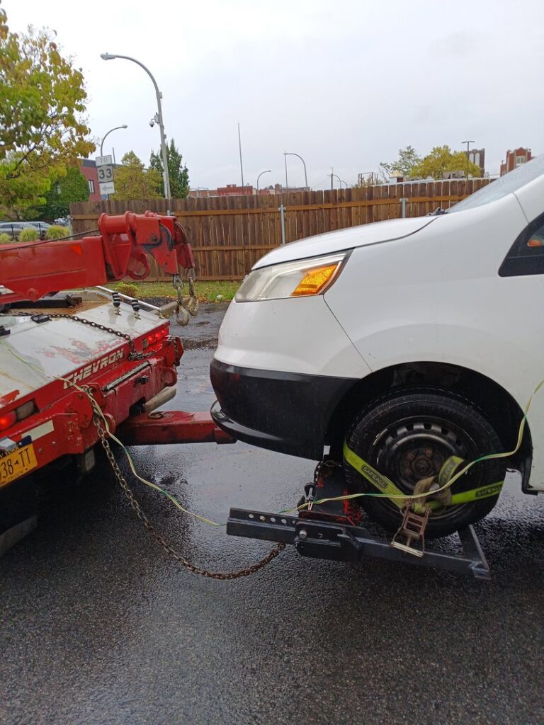 A white van being towed by a red tow truck using a wheel lift system, provided by Buffalo Towing Services in Buffalo, NY.