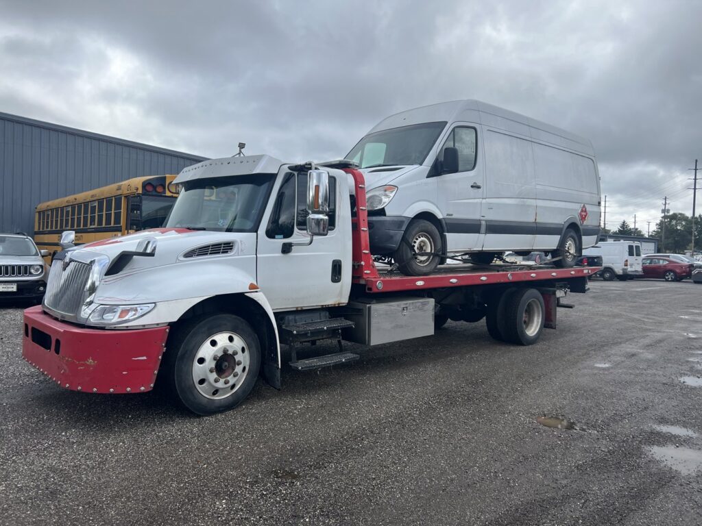 A white van being transported on a flatbed tow truck by Quiñones Towing in Cleveland, OH.