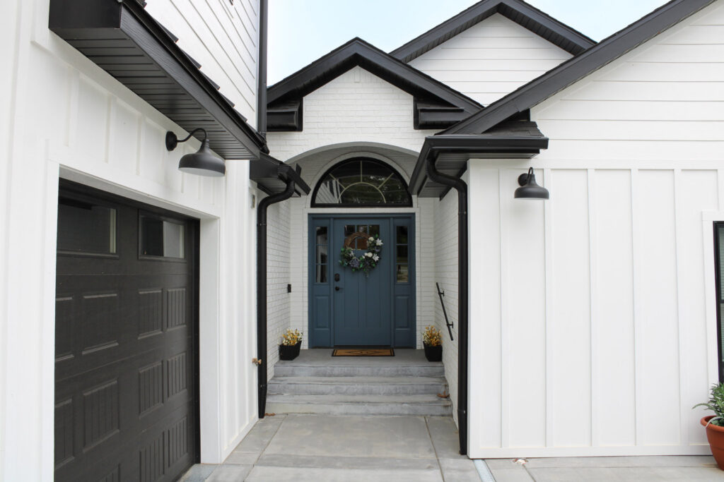 The inviting front entrance of a white home with modern vertical siding and black trim by Xtreme Exteriors in Rogers, AR.