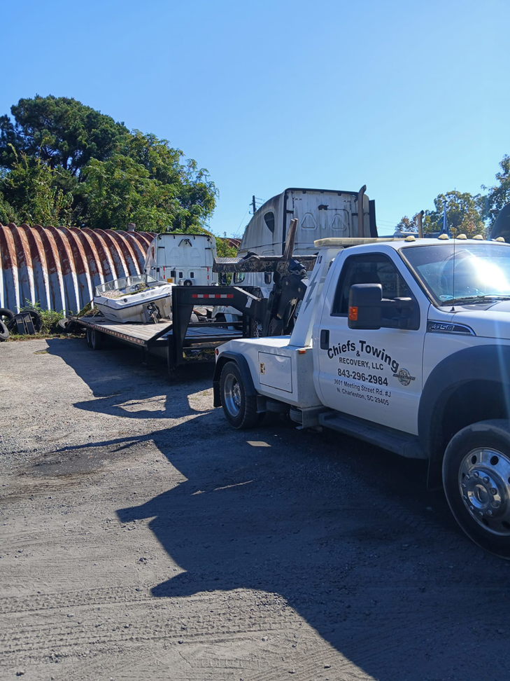 A white wrecker tow truck from Towing services towing a flatbed trailer with a load in North Charleston, SC.