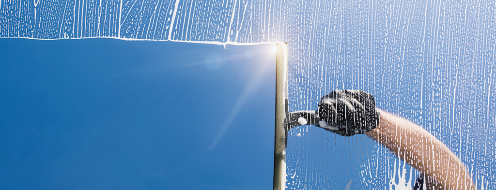 A gloved hand uses a squeegee to clean a window, showing suds, for Glory Cleaning Service in Irvine, CA.