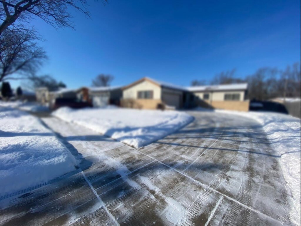A cleared residential driveway with tire tracks in the snow, showcasing snow removal service by Evo Lawn & Landscape LLC in Waukegan, IL.