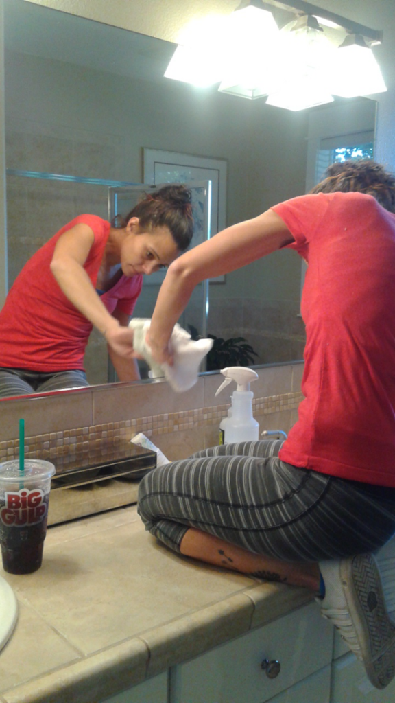 A professional house cleaner from JLCleaning meticulously cleaning a bathroom mirror and countertop in Beaverton, OR.