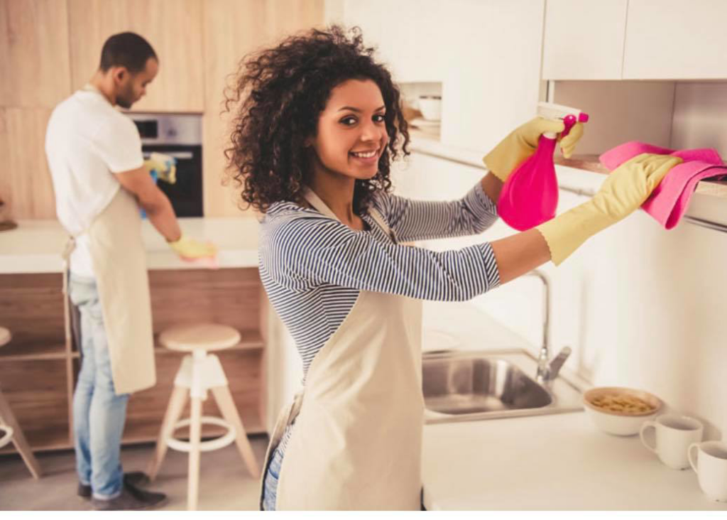 A woman wearing gloves and an apron cleaning kitchen cabinets for Ariana cleaning services in Fort Lauderdale, FL