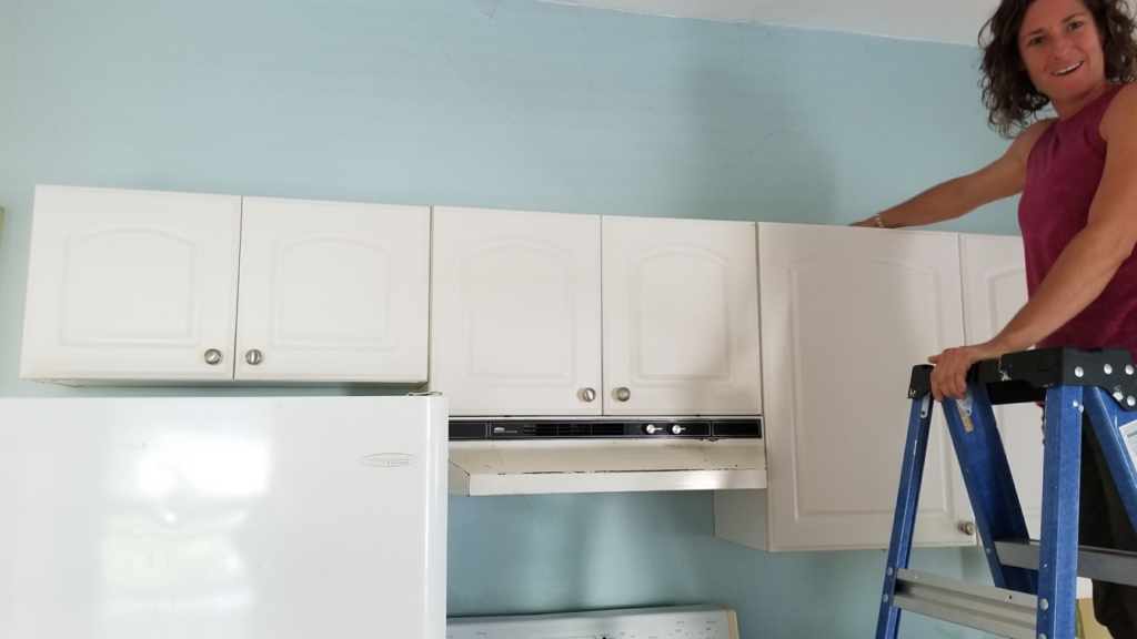 A professional cleaner on a ladder cleaning kitchen cabinets and range hood for Simply Clean Professional Cleaning Services LLC in Rutland, VT.
