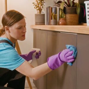 A professional house cleaner from Your Green Clean Crew in Bellevue, WA, wiping down kitchen cabinets with a spray bottle and cloth.