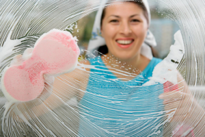 A smiling woman cleaning a window with a sponge, viewed through the soapy glass, by Super Clean in Honolulu, HI