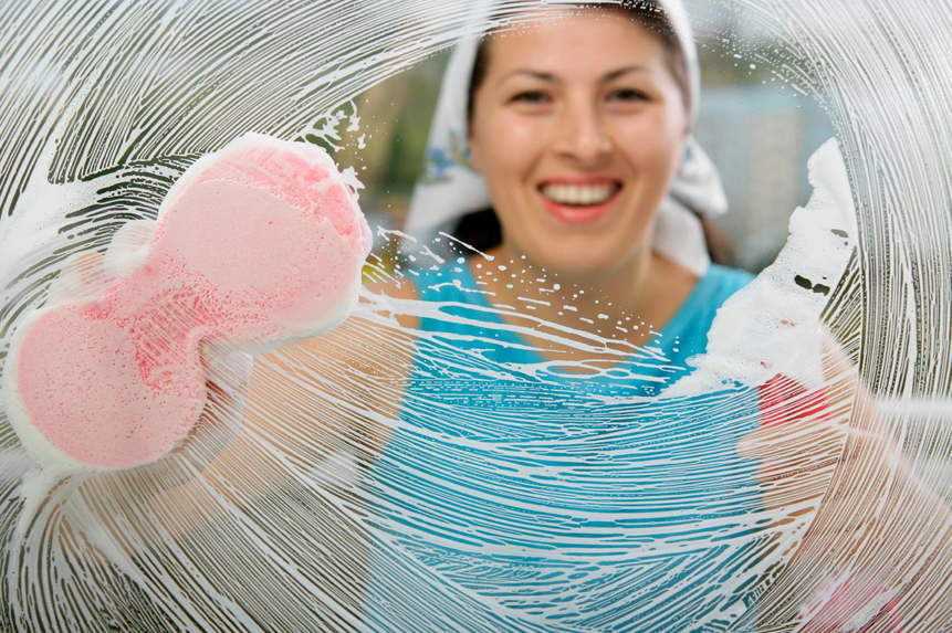 A smiling woman cleaning a window with a sponge, viewed through the soapy glass, by Super Clean in Honolulu, HI