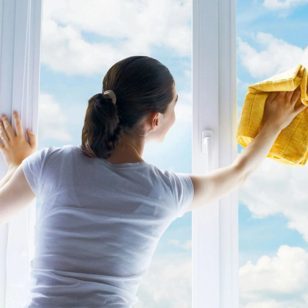 A woman cleaning a window with a yellow cloth, showing sparkling results for Clean Home Nash in Nashville, TN.