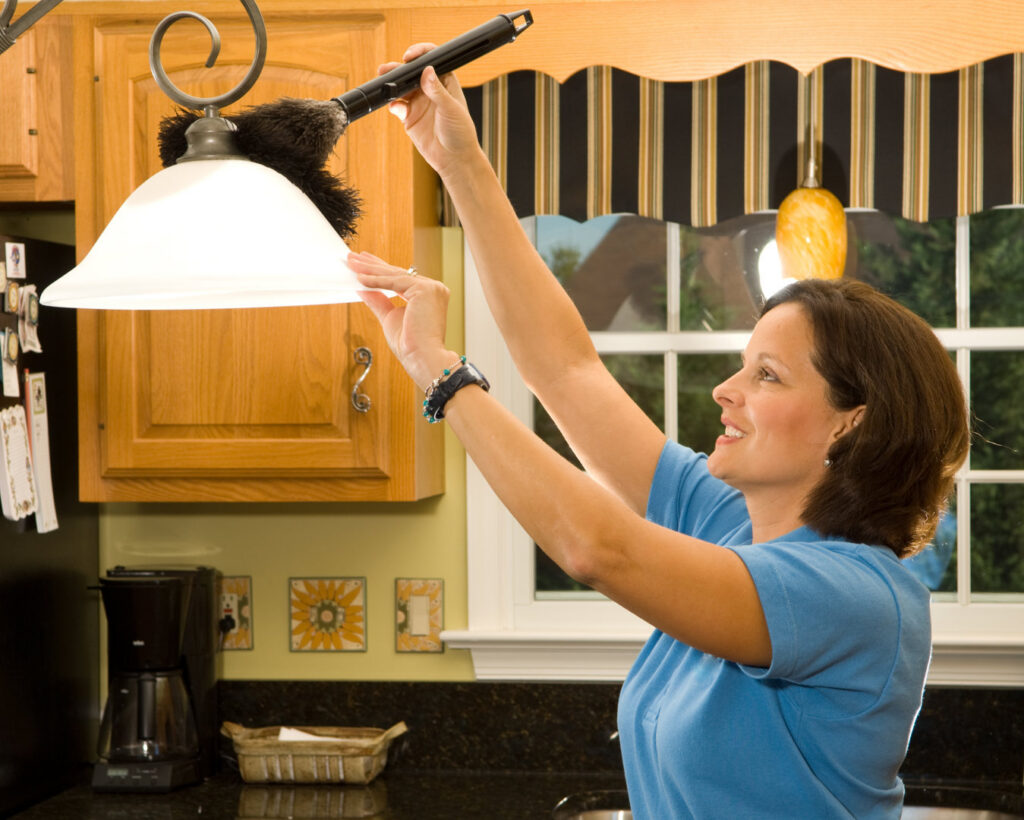 A woman dusting a light fixture above a kitchen counter, performing house cleaning services for Mariahs House cleaning in Renton, WA.