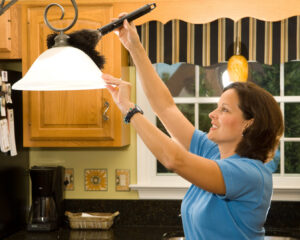 A woman dusting a light fixture above a kitchen counter, performing house cleaning services for Mariahs House cleaning in Renton, WA.