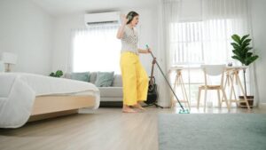 A woman wearing headphones and mopping a wooden floor in a home, depicting house cleaning services by Cascade Fresh Cleaning Services in Grand Rapids, MI.