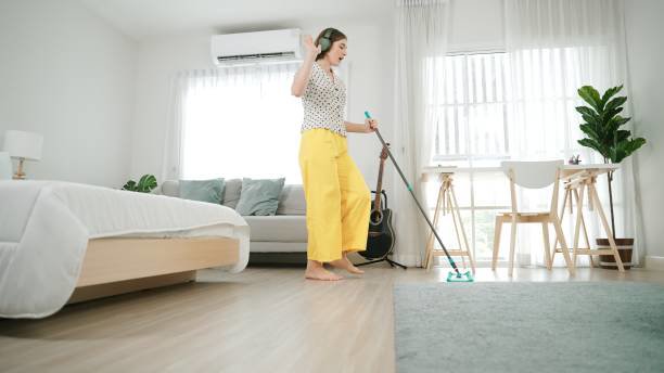 A woman wearing headphones and mopping a wooden floor in a home, depicting house cleaning services by Cascade Fresh Cleaning Services in Grand Rapids, MI.