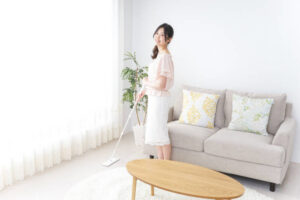 A woman smiling while mopping a wooden floor in a bright living room, illustrating house cleaning services by Cascade Fresh Cleaning Services in Grand Rapids, MI.