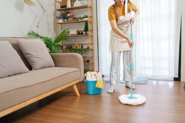 A woman mopping a wooden floor with a bucket of cleaning supplies nearby, illustrating house cleaning by Cascade Fresh Cleaning Services in Grand Rapids, MI.