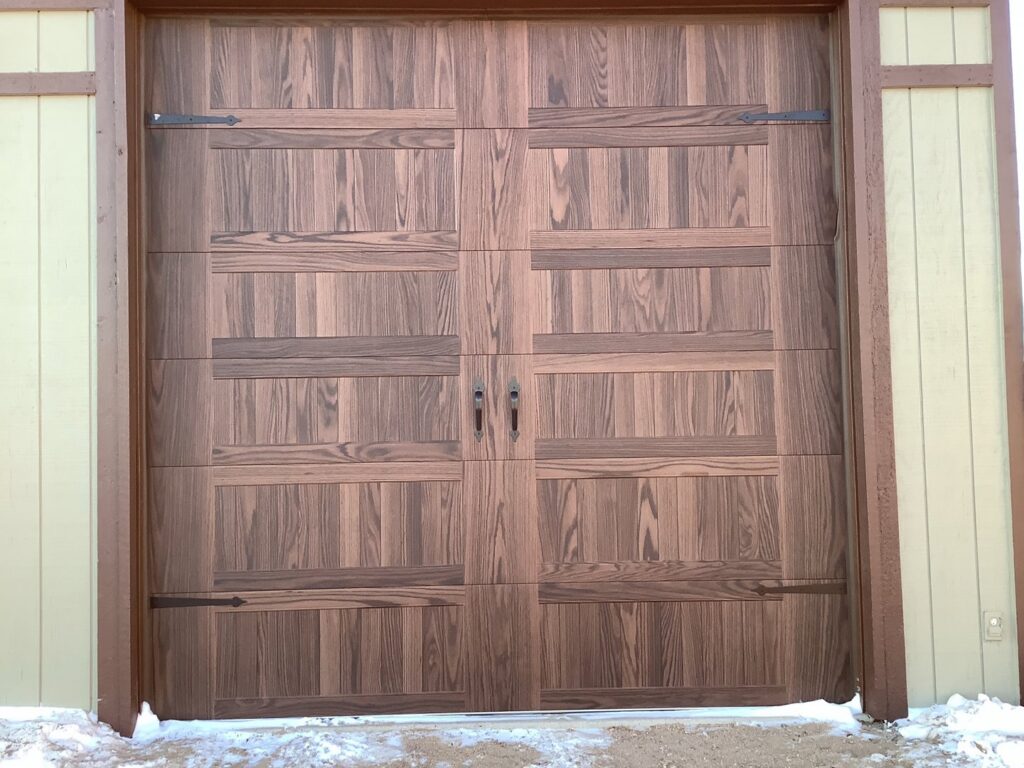 A dark wood-look garage door with decorative hardware installed on a house by Apex Garage Doors in Columbus, OH.