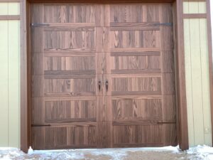 A dark wood-look garage door with decorative hardware installed on a house by Apex Garage Doors in Columbus, OH.