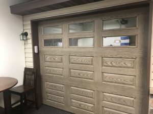 A wood-look garage door with windows on display, offered by Up N Over Garage Doors LLC in Layton, UT.