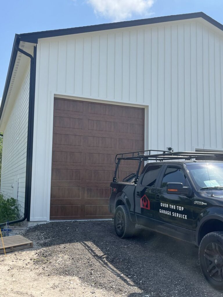 A new wood-look garage door installed on a white building, with an Over The Top Garage Service truck nearby in Albuquerque, NM.