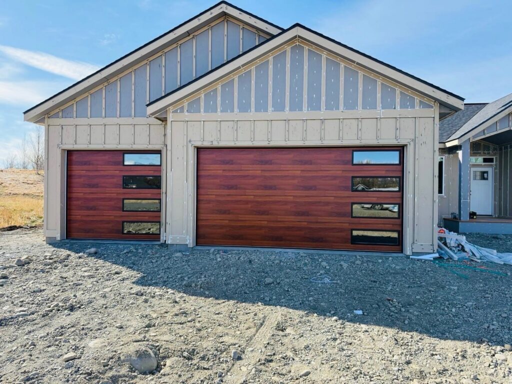 Two beautiful wood-look garage doors with modern windows installed on a residential property by Elite Doors in Wasilla, AK.