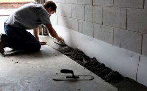 A worker applying waterproofing sealant along a basement wall for Waterdry Indiana in South Bend, IN