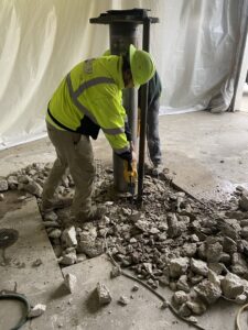A worker from DeCarlo Demolition Company breaking up concrete around a pillar with a jackhammer in Des Moines, IA.