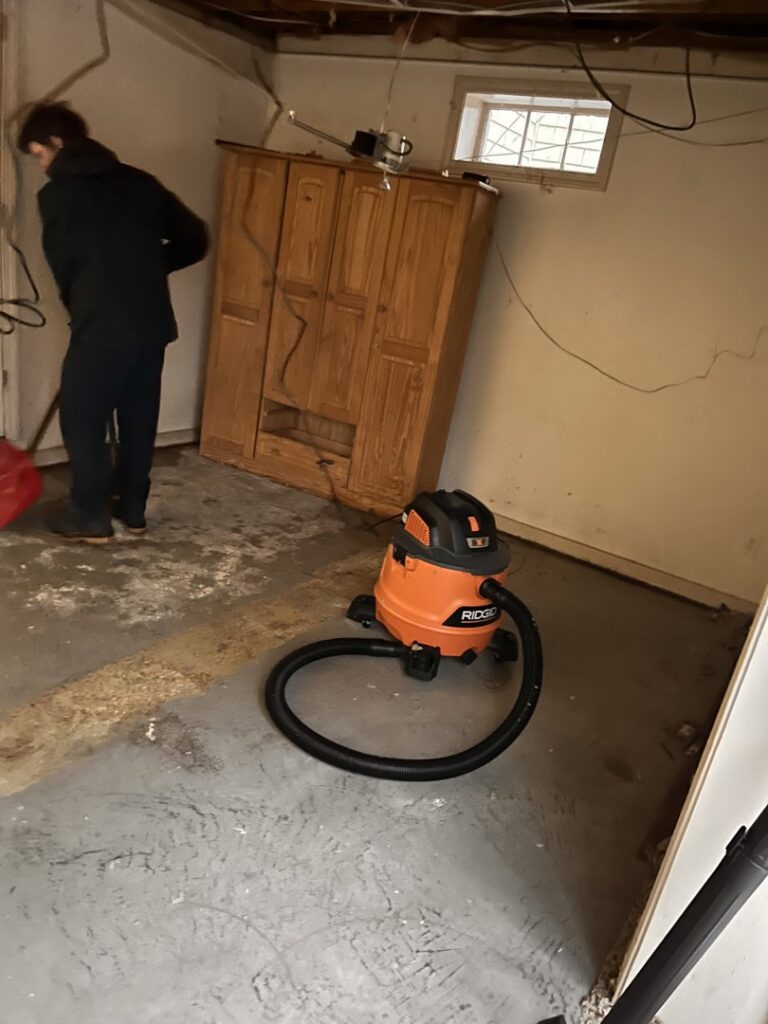 A Paul Davis Restoration of Greater Portland, ME worker cleaning a basement floor with a shop vacuum.