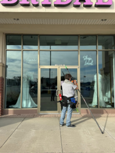 A worker from Rocket Window Cleaning in Lincoln, NE, cleaning the exterior windows of a commercial building with a long pole.