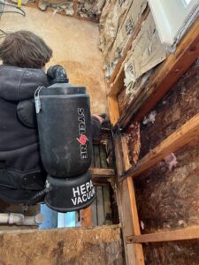 A worker using a backpack vacuum to clean a water-damaged wall with exposed studs for Utah Home Restoration in Springville, UT