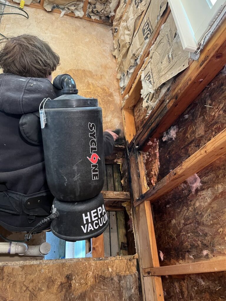 A worker using a backpack vacuum to clean a water-damaged wall with exposed studs for Utah Home Restoration in Springville, UT