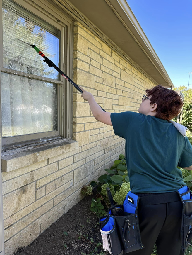 A worker from Rocket Window Cleaning in Lincoln, NE, cleaning an exterior window of a residential home with a long pole.