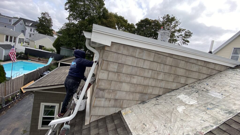 A worker from Empire Pro Painting Inc. cleaning gutters on a residential home in Lynn, MA, a key service for water damage prevention.